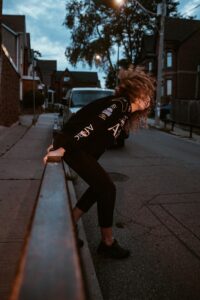 Woman in stylish streetwear captured in motion on an urban street at dusk.